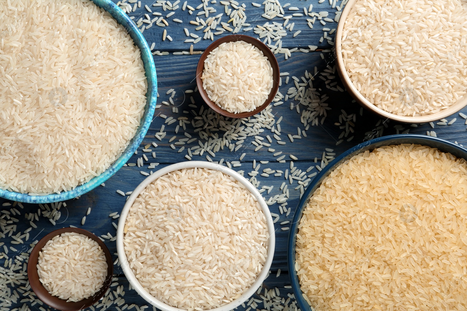 Photo of Flat lay composition with different types of rice in bowls on color wooden background