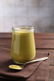 Glass jar and spoon with tasty mustard sauce on wooden table