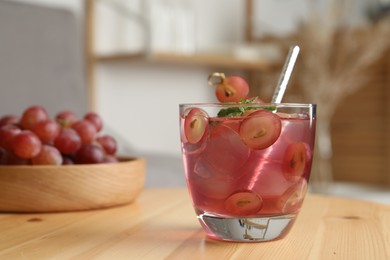 Photo of Refreshing drink with soda water, grapes, ice and mint on wooden table indoors. Space for text