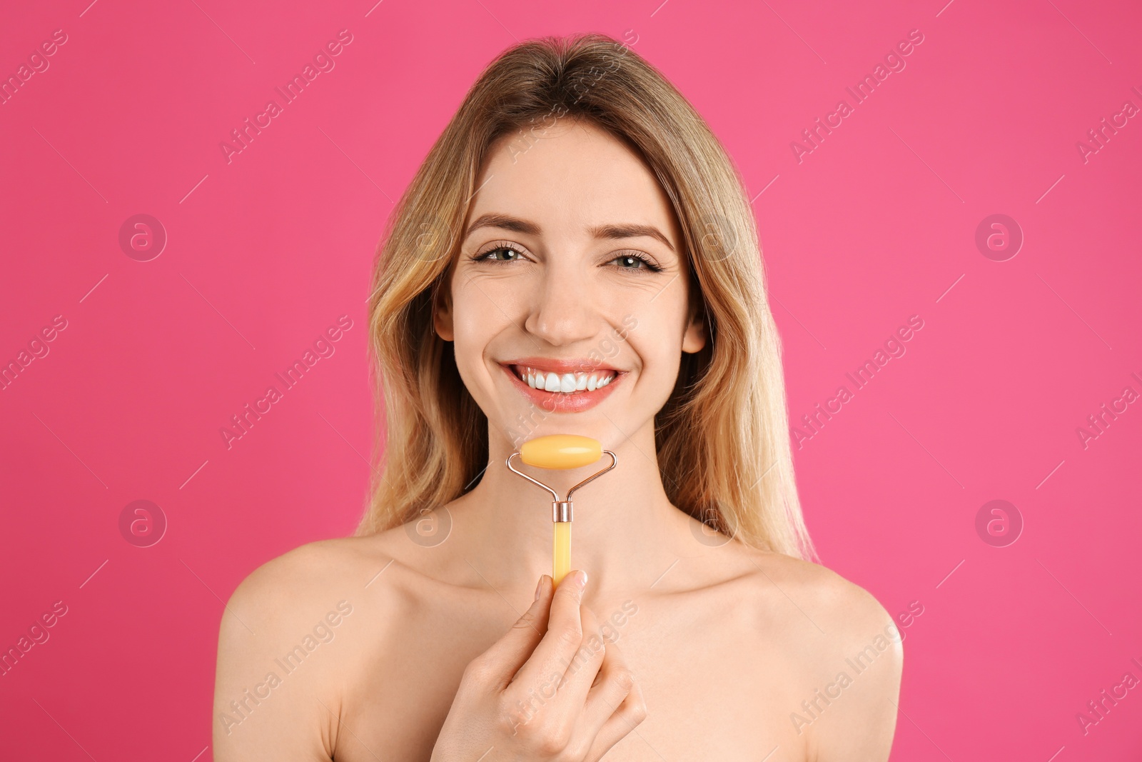 Photo of Young woman using natural jade face roller on pink background