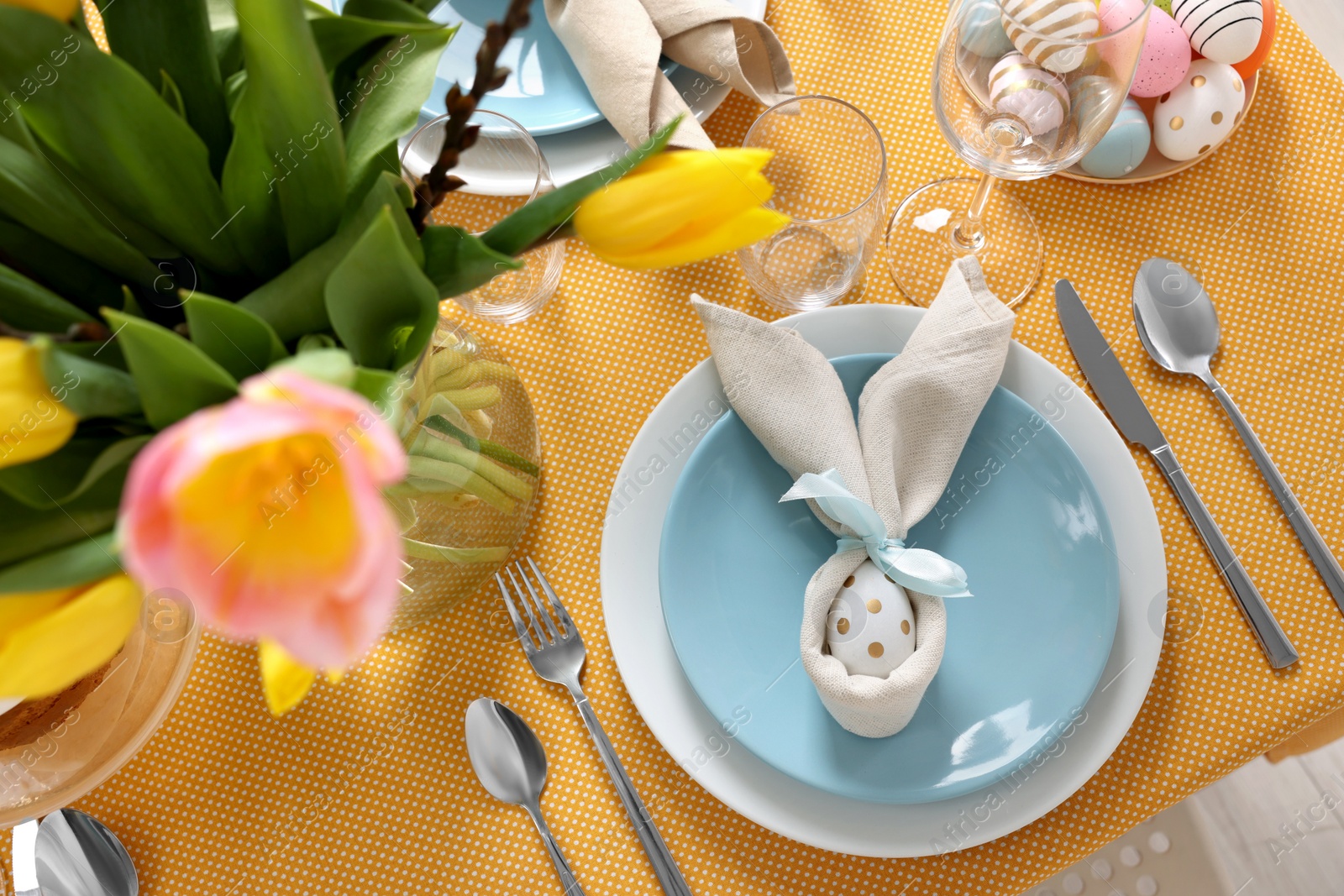 Photo of Festive table setting with painted eggs, plate and vase of tulips, view from above. Easter celebration