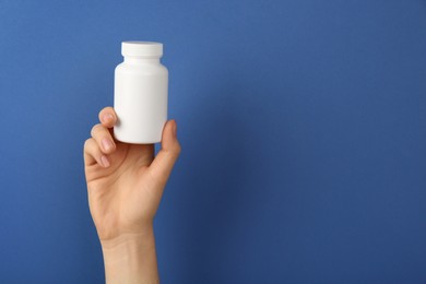 Photo of Woman holding blank white jar of vitamins on blue background, closeup. Space for text