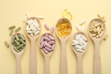 Different vitamin pills in spoons on pale yellow background, flat lay
