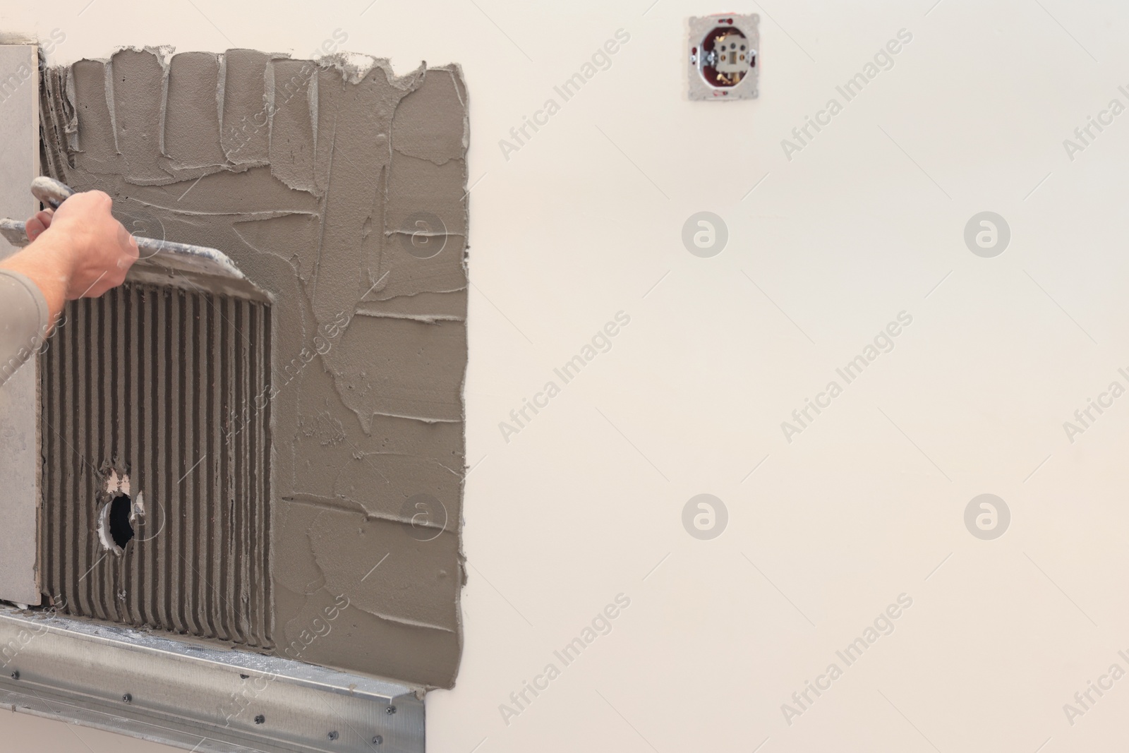 Photo of Worker spreading adhesive mix on wall for tile installation indoors, closeup