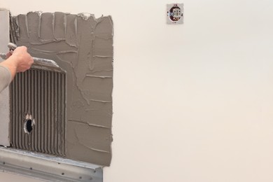 Photo of Worker spreading adhesive mix on wall for tile installation indoors, closeup