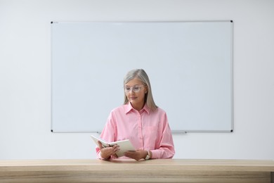 Photo of Professor with book sitting at desk in classroom