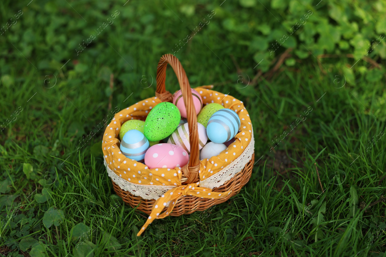 Photo of Easter celebration. Painted eggs in wicker basket on green grass