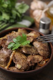 Tasty fried chicken liver with onion and parsley in bowl on table, closeup