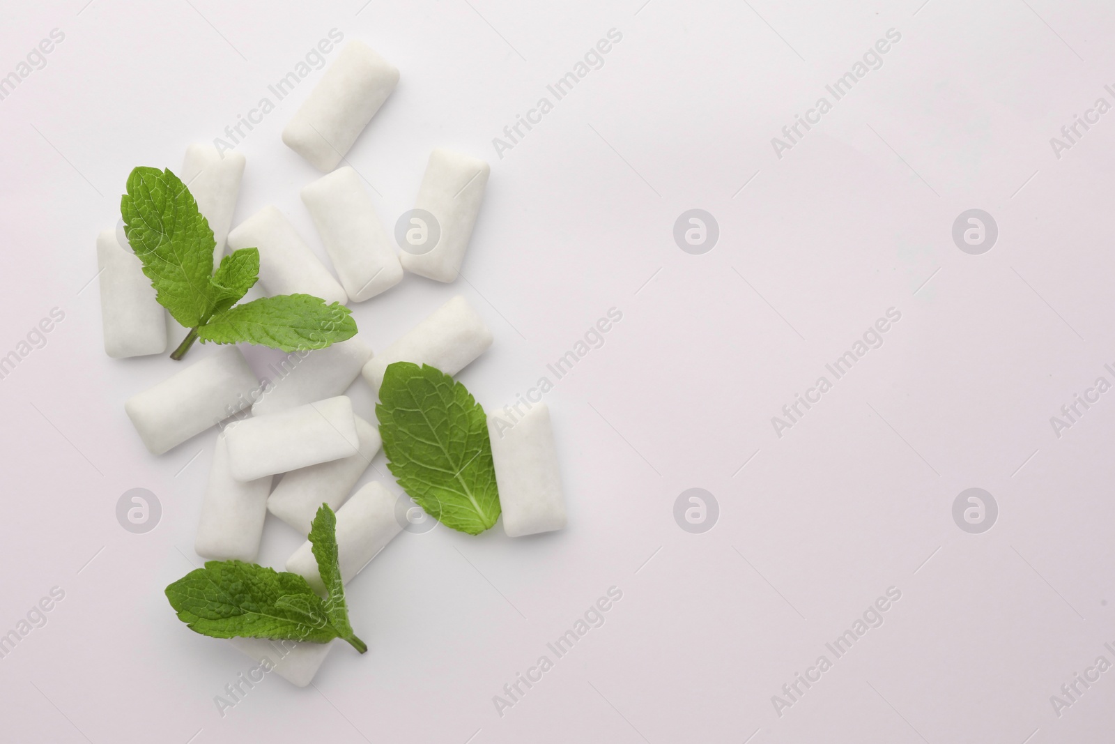 Photo of Tasty chewing gums and mint leaves on white background, top view. Space for text