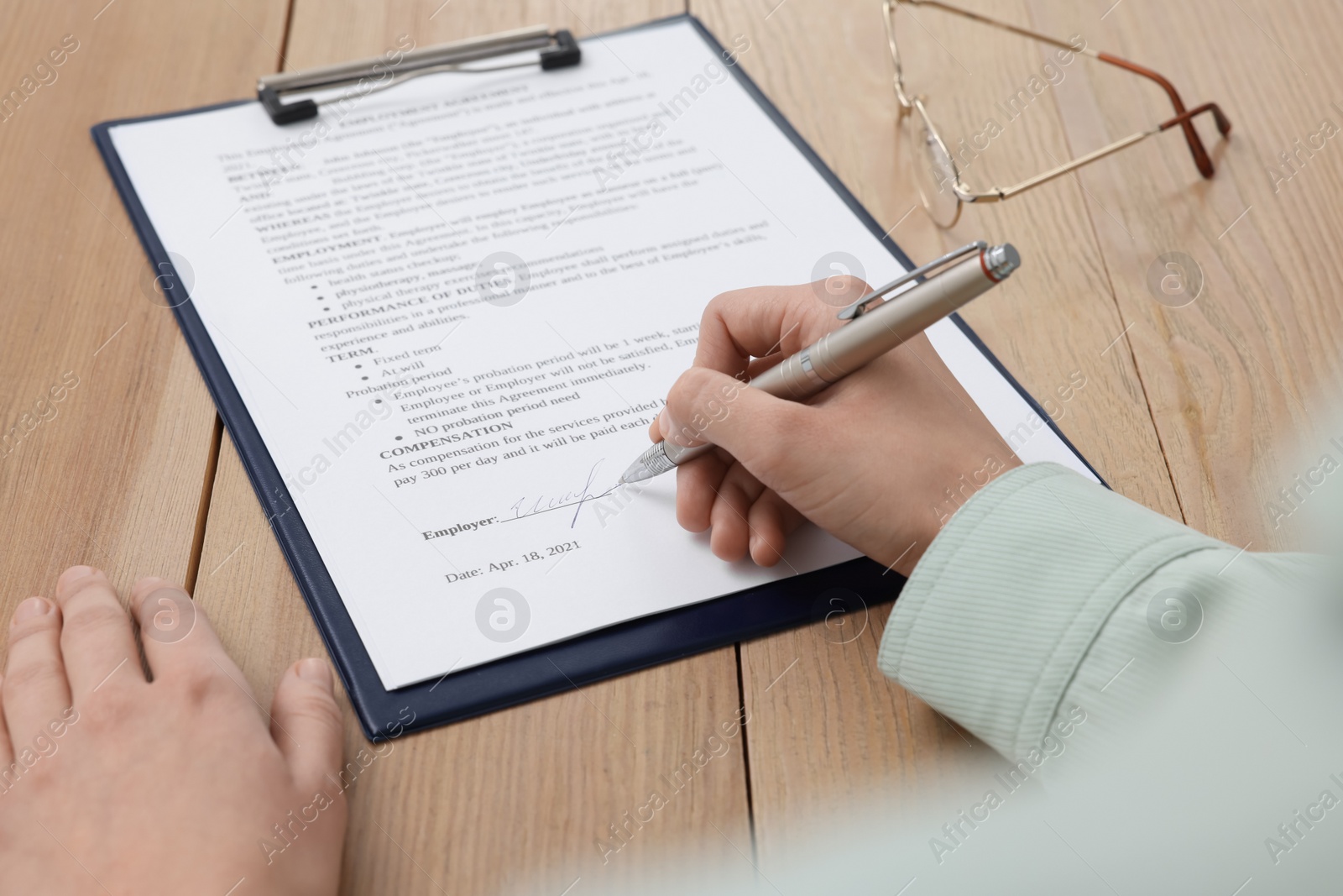 Photo of Woman signing contract at wooden table, closeup.