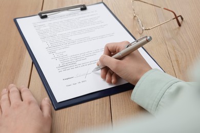 Woman signing contract at wooden table, closeup.