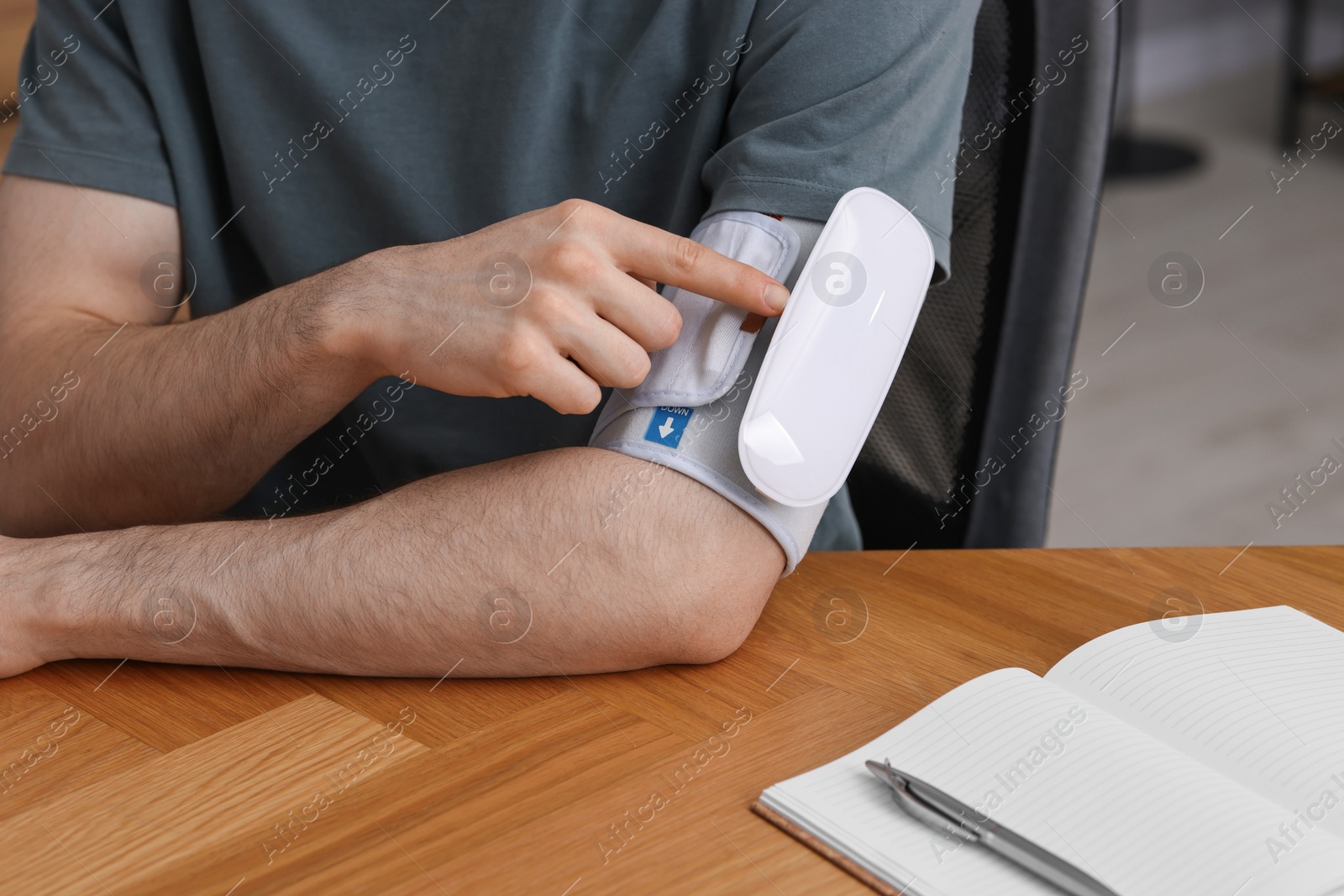 Photo of Man measuring his blood pressure with tonometer at wooden table indoors, closeup