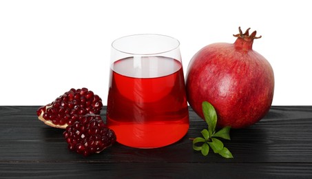 Photo of Refreshing pomegranate juice in glass, leaves and fruits on black wooden table against white background