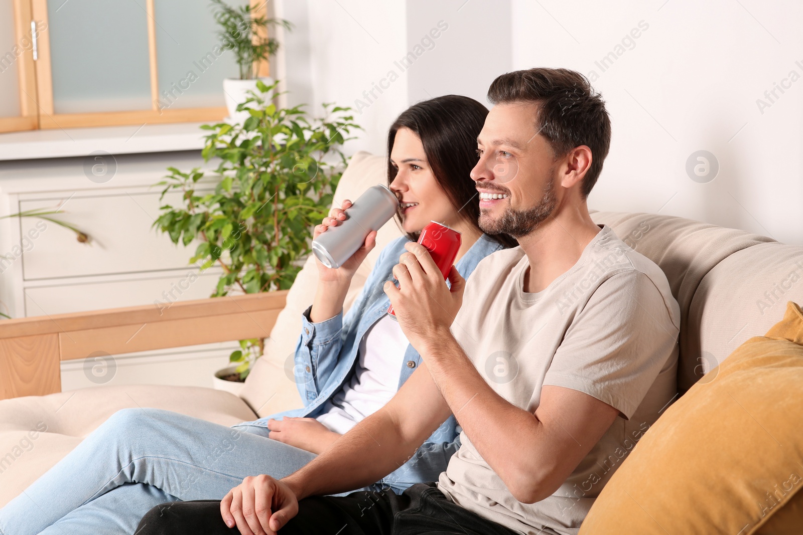 Photo of Happy couple drinking beverages on sofa indoors