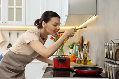 Photo of Woman tasting fresh bouillon in kitchen. Homemade recipe