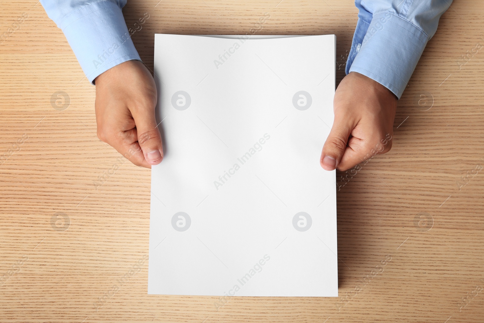 Photo of Man holding blank paper sheets for brochure at wooden table, top view. Mock up