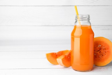 Tasty pumpkin juice in glass bottle and cut pumpkin on white wooden table. Space for text