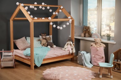 Photo of Stylish child room interior with wooden bed in shape of house and toys