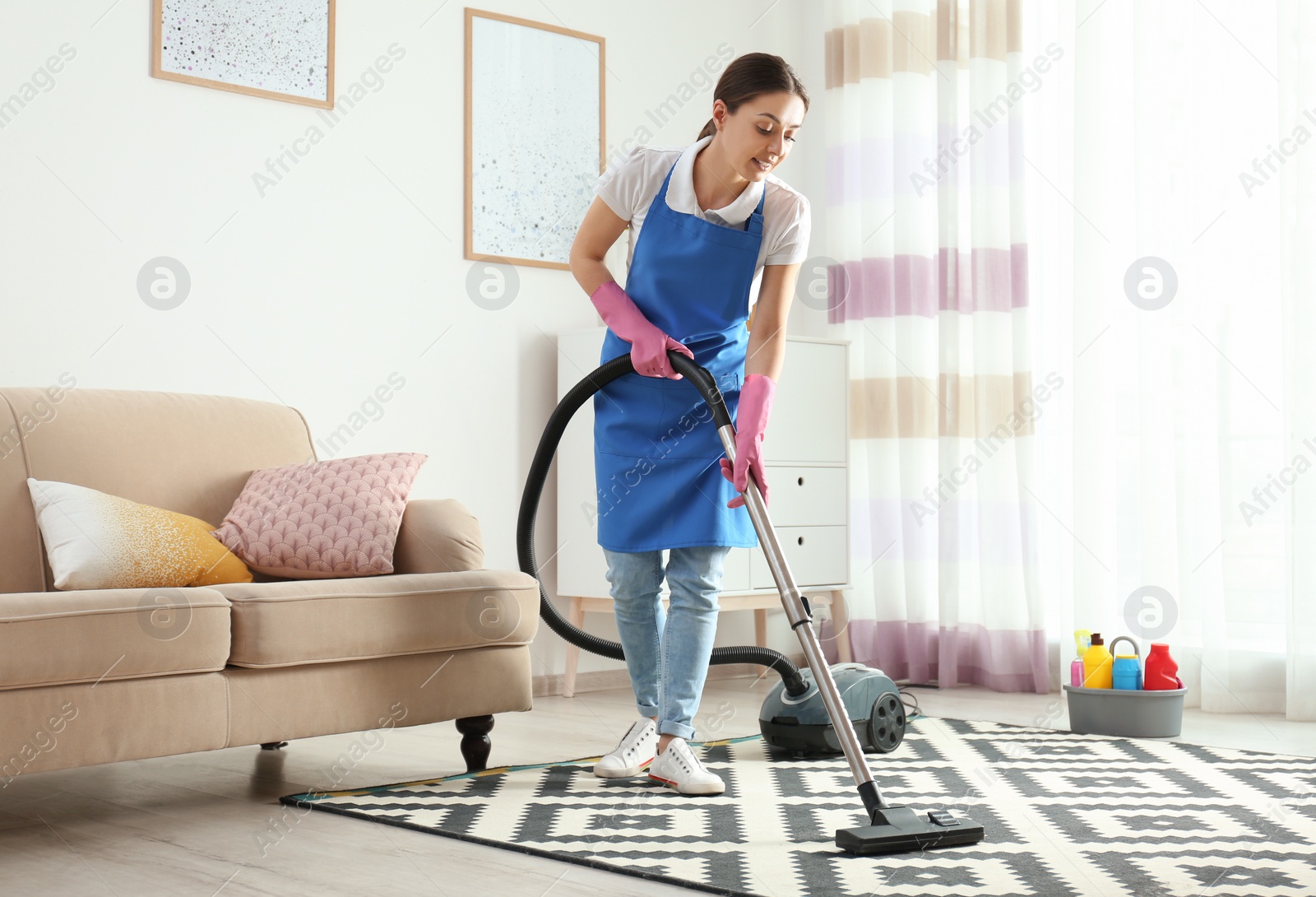 Photo of Woman hoovering carpet in living room. Cleaning service