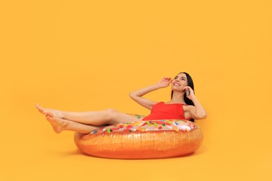Photo of Happy young woman with beautiful suntan talking by phone on inflatable ring against orange background