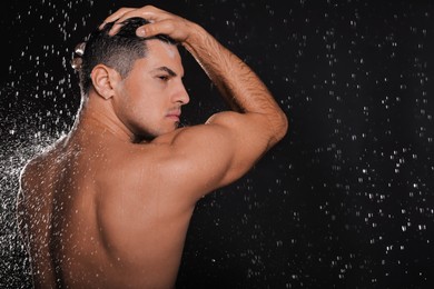 Photo of Man washing hair while taking shower on black background. Space for text