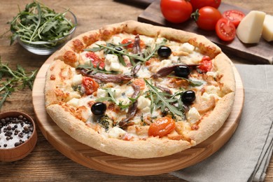 Tasty pizza with anchovies and ingredients on wooden table