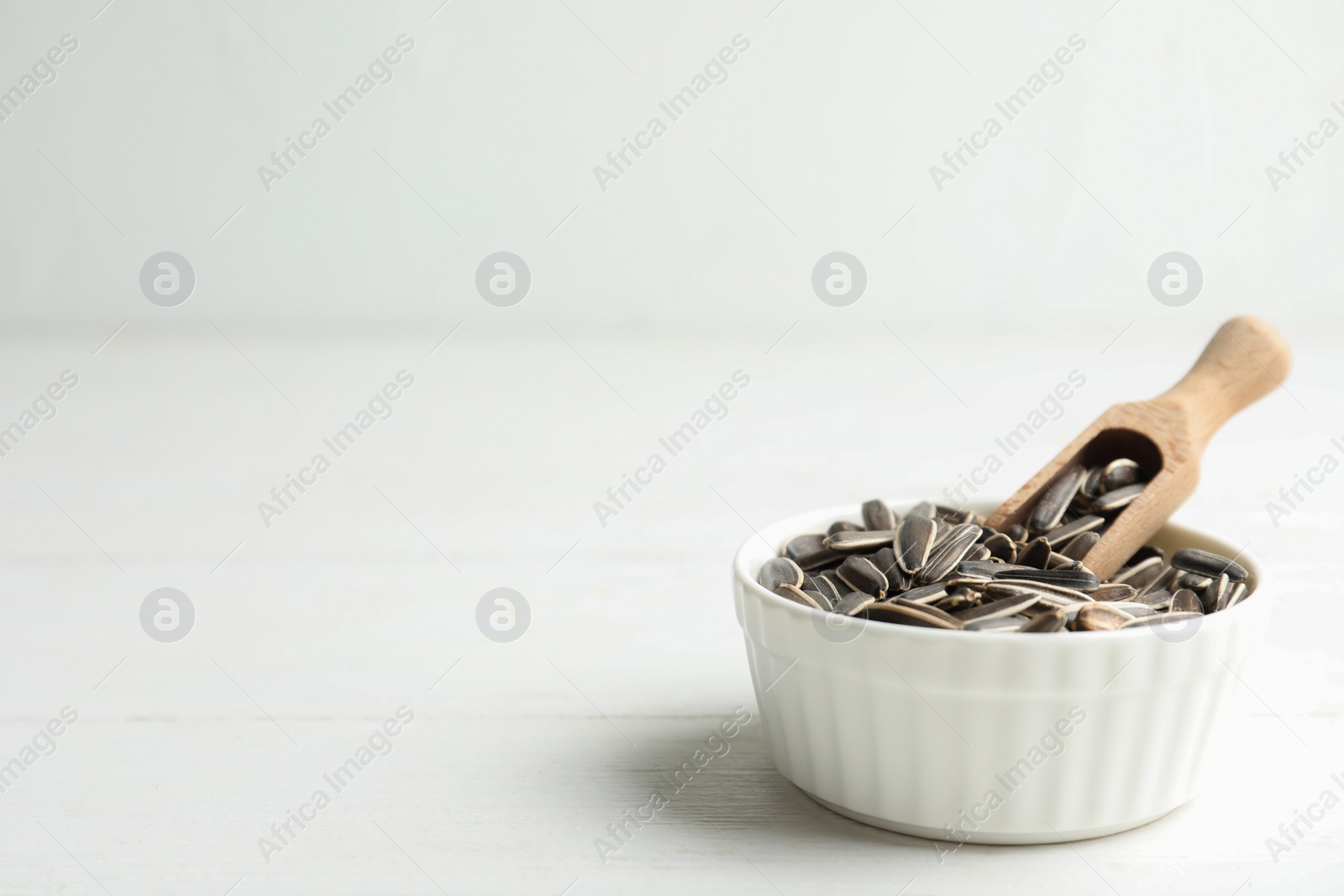 Photo of Organic sunflower seeds on white wooden table. Space for text