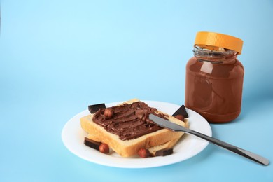 Photo of Tasty toast with chocolate paste and nuts near jar of cream on light blue background