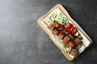 Photo of Delicious shish kebabs with vegetables and lavash on grey table, top view. Space for text