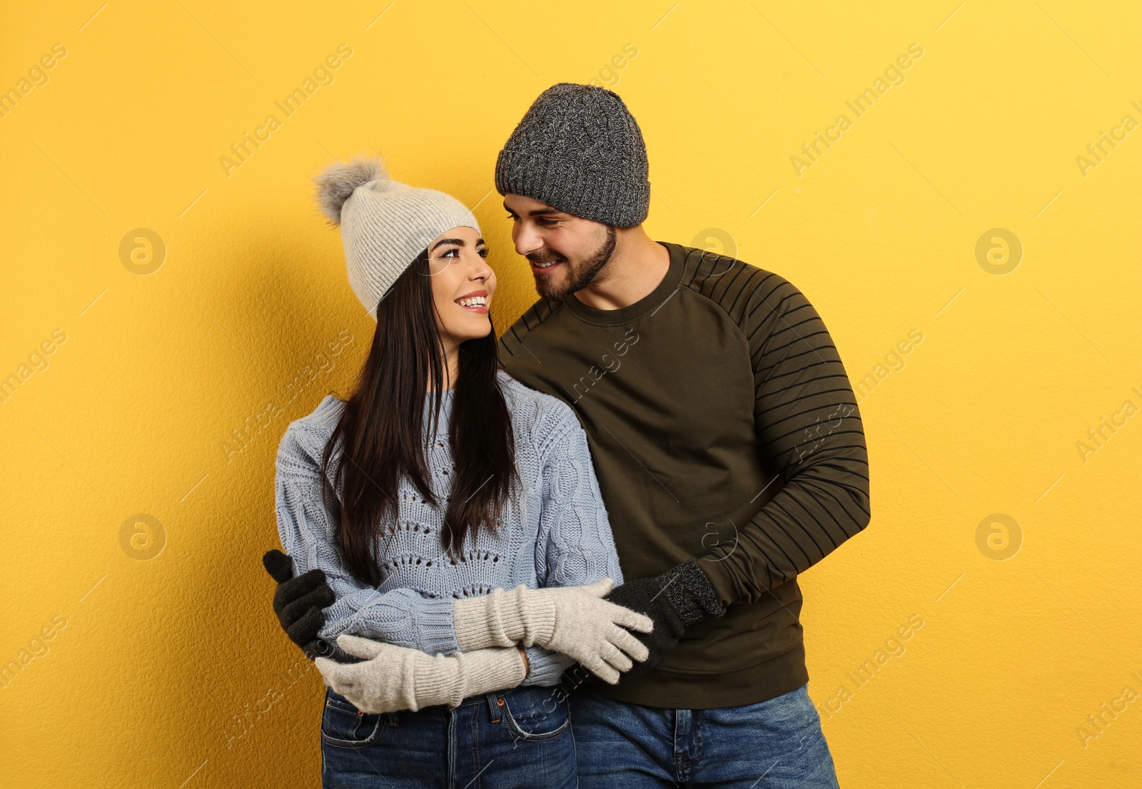 Photo of Happy young couple in warm clothes on yellow background. Winter vacation