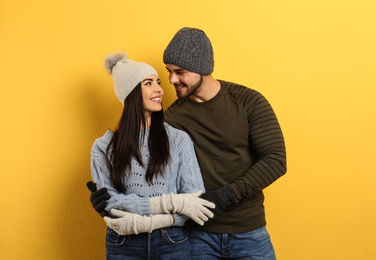 Happy young couple in warm clothes on yellow background. Winter vacation