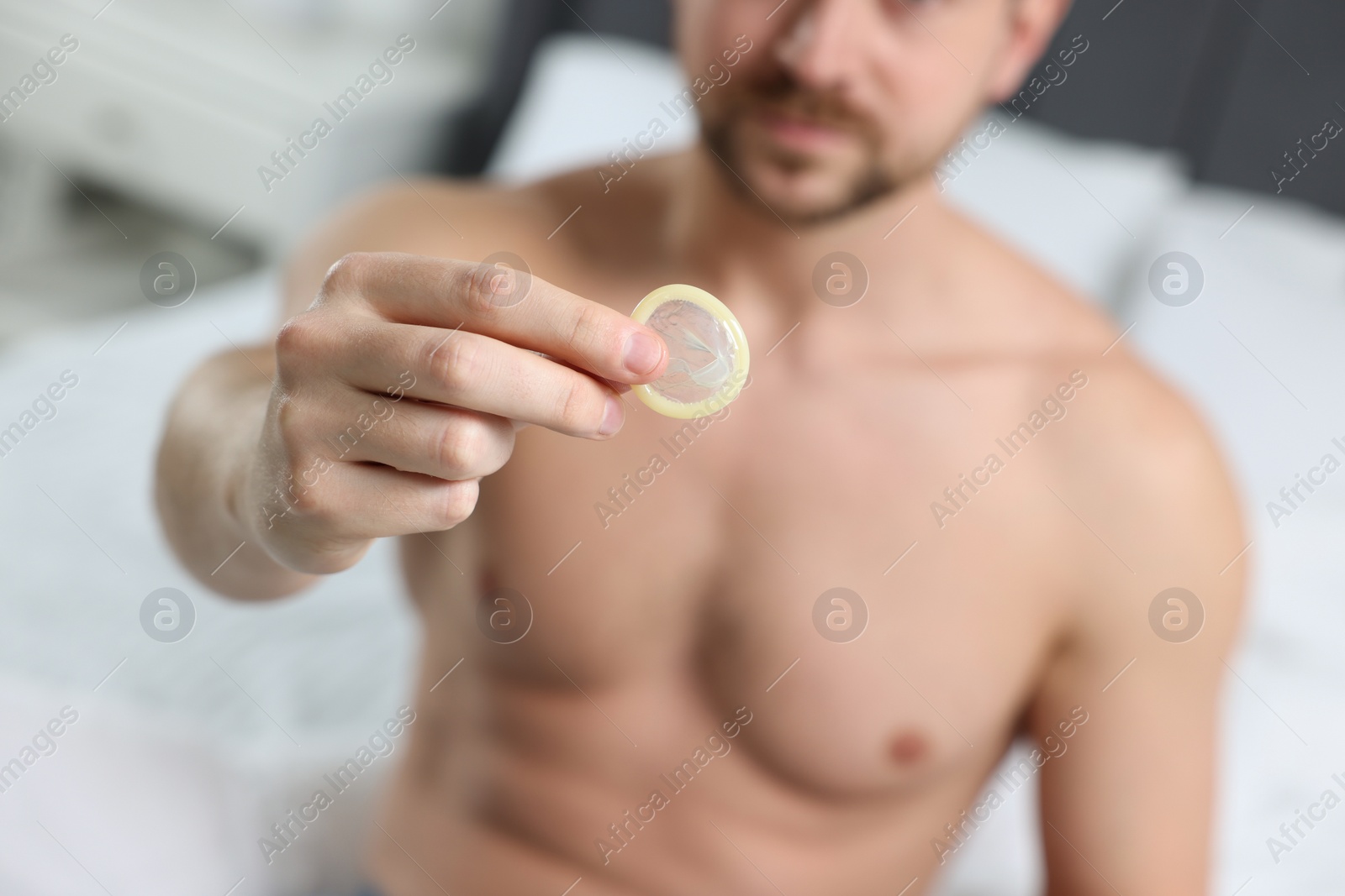 Photo of Closeup view of man showing condom on bed