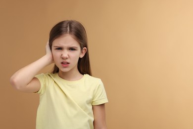 Photo of Hearing problem. Little girl suffering from ear pain on pale brown background, space for text