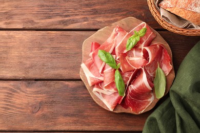 Photo of Slices of tasty cured ham, basil and bread on wooden table, flat lay. Space for text
