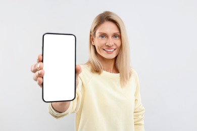 Happy woman holding smartphone with blank screen on white background