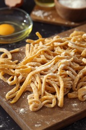 Photo of Board with homemade pasta and flour on dark table, closeup