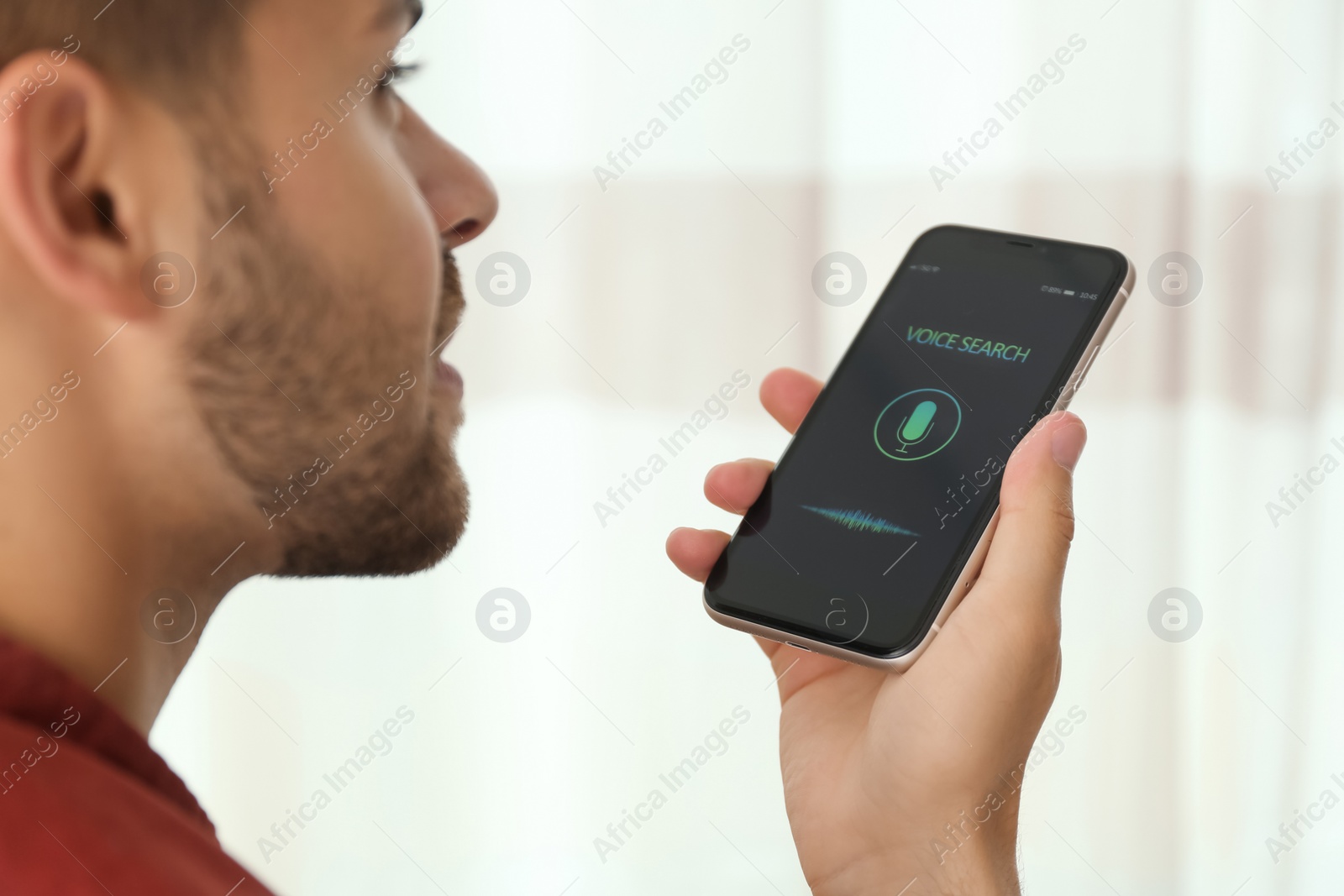 Photo of Young man using voice search on smartphone indoors, closeup