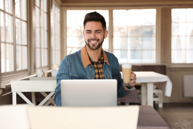 Photo of Young blogger with laptop drinking latte at table in cafe