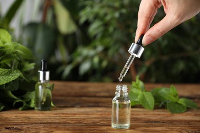 Photo of Woman dripping mint essential oil into bottle at wooden table, closeup. Space for text