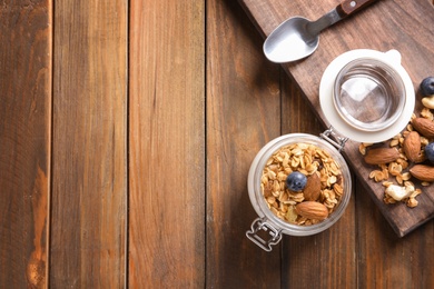 Photo of Jar with yogurt, nuts and granola on wooden table, top view