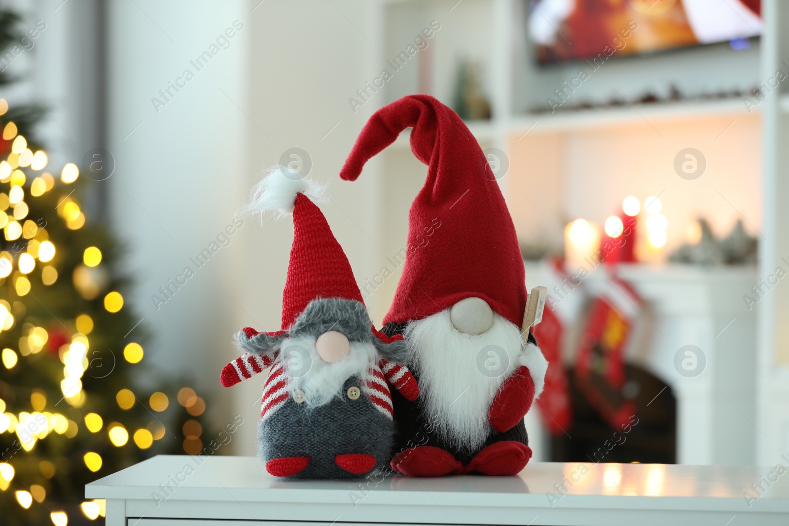 Photo of Funny Christmas gnomes on table in room with festive decoration