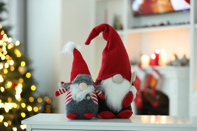 Photo of Funny Christmas gnomes on table in room with festive decoration