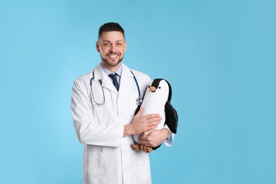 Photo of Pediatrician with toy penguin and stethoscope on light blue background