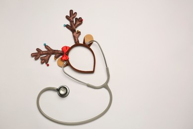 Greeting card for doctor with stethoscope and reindeer headband on white background, flat lay. Space for text