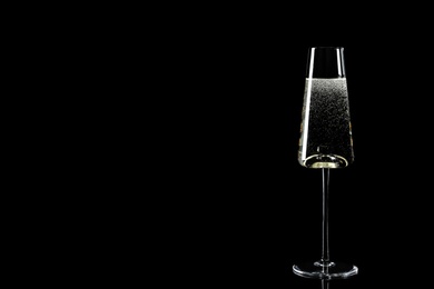 Glass of champagne on black background, space for text