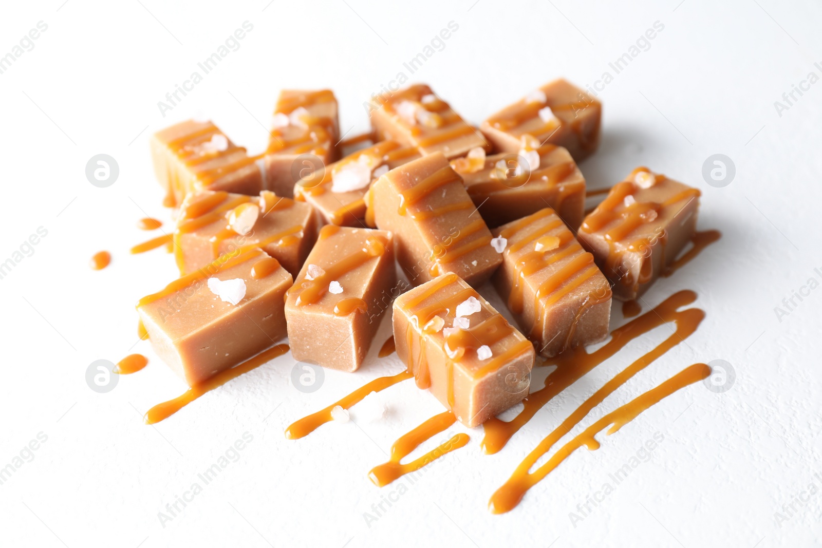 Photo of Tasty candies, caramel sauce and salt on white table