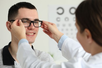 Photo of Vision testing. Ophthalmologist giving glasses to young man indoors