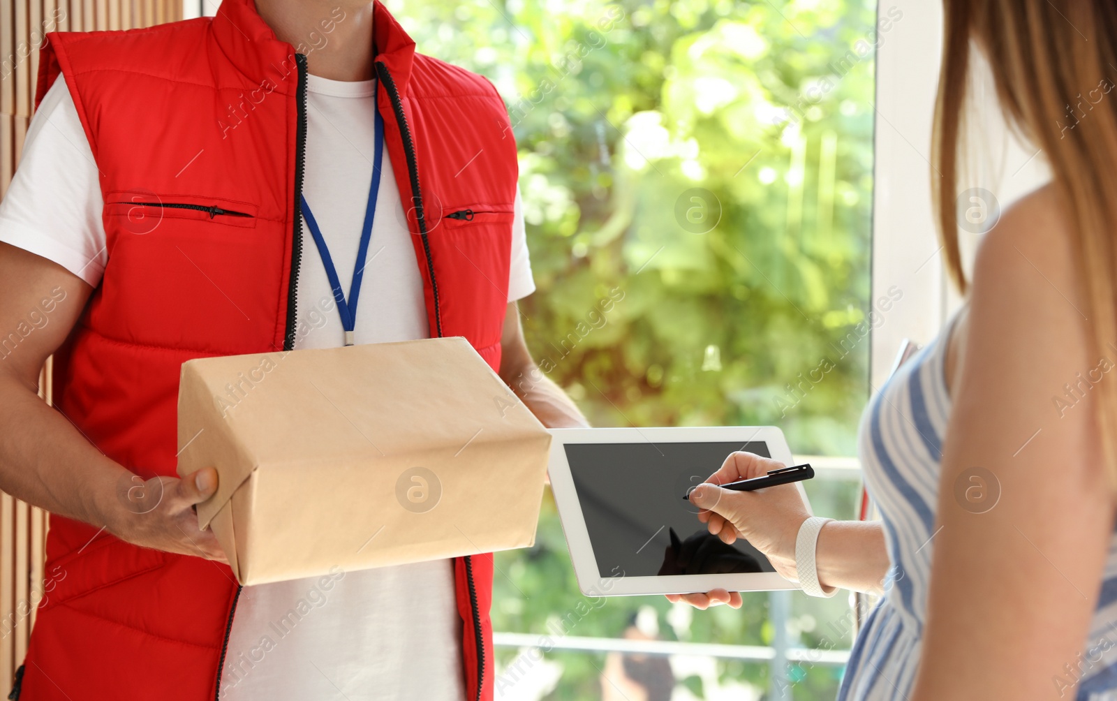 Photo of Young courier with parcel and client signing on tablet indoors, closeup