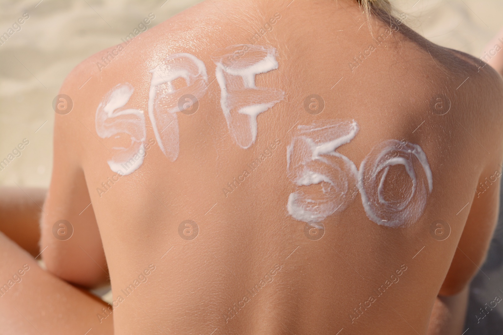 Photo of Child with abbreviation SPF 50 of sunscreen on back at beach, closeup