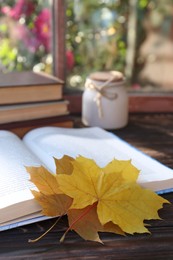 Photo of Books, candle and beautiful leaves as bookmark on wooden table